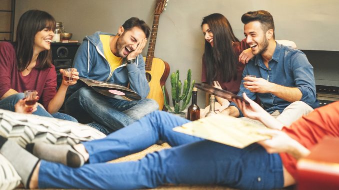 Happy young friends having fun at home listening vintage vinyl disc music in living room - Group of people enjoying their time in apartment drinking shots and laughing